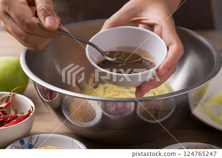 Spicy mango salad cooking, Hand adding fermented fish in bowl and mixing with ingredients Spicy mango salad cooking, Hand adding fermented fish in bowl and mixing with ingredients 124765247