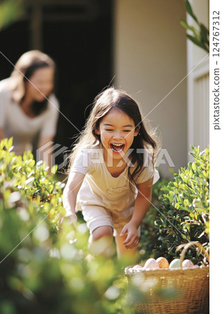 Laughing girl running to wisker basket full of Easter eggs in countryard. Large Easter eggs hunt. 124767312