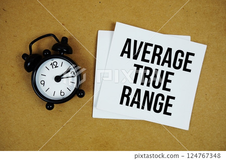 Average True Range text on sticky note with alarm clock on paper craft background 124767348