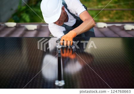 Worker building photovoltaic solar panel system on rooftop of house. Close up of man engineer in helmets and gloves installing solar module with help of hex key outdoors. Renewable energy. 124768663
