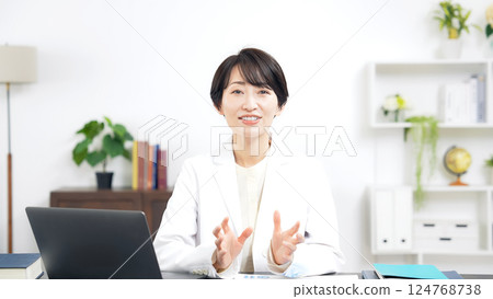 A middle-aged woman in a white coat talking to the camera 124768738