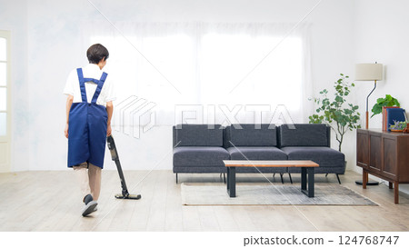A middle-aged woman wearing an apron vacuuming the floor of a room 124768747