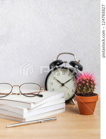 Eyeglasses resting on stack of notebooks with pen, alarm clock, and cactus Eyeglasses resting on stack of notebooks with pen, alarm clock, and cactus 124768827