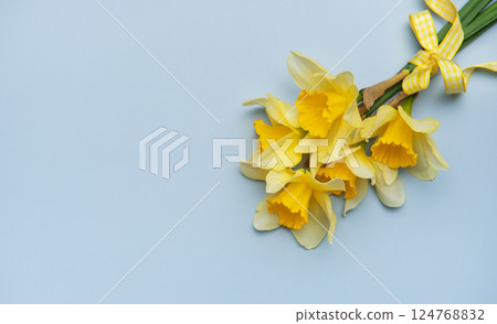 Bouquet of yellow daffodils with ribbon lying on pastel blue background Bouquet of yellow daffodils with ribbon lying on pastel blue background 124768832