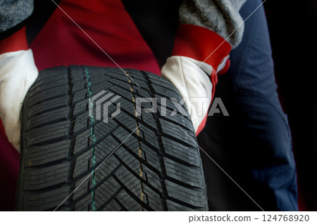Close-up of mechanic's gloved hands inspecting tire, highlighting tread patterns and automotive care 124768920