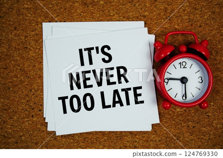 It's Never Too Late text on sticky note with alarm clock on cork paper background 124769330