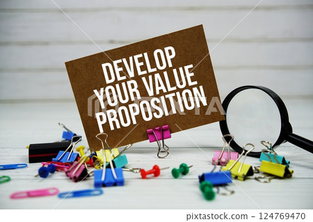Develop Your Value Proposition text on paper card with magnifying glass and stationary on wooden background 124769470