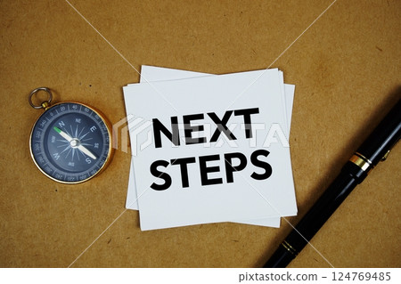 Next Steps text on sticky note with compass and pen on paper craft background 124769485