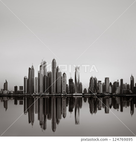Monochrome city skyline with tall skyscrapers reflecting on calm water under a cloudy sky, Dubai Marina bay UAE Monochrome city skyline with tall skyscrapers reflecting on calm water under a cloudy sky, Dubai Marina bay UAE 124769895