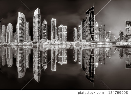 Urban city skyline with illuminated skyscrapers and waterfront railing in black and white at night, Dubai Marina bay UAE 124769908