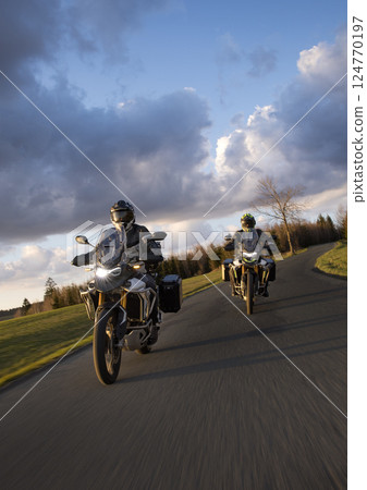 Drivers riding motorcycle on empty road during sunset, spring mountains Drivers riding motorcycle on empty road during sunset, spring mountains 124770197