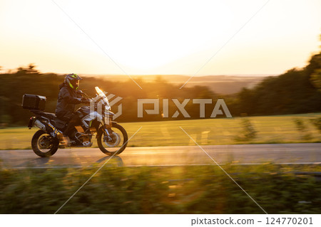 Driver riding motorcycle on empty road during sunset, spring mountains 124770201