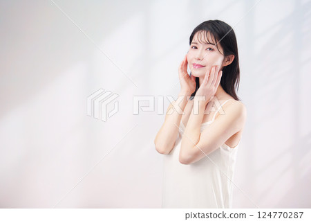 A young woman smiling and taking care of her skin (simple background) 124770287