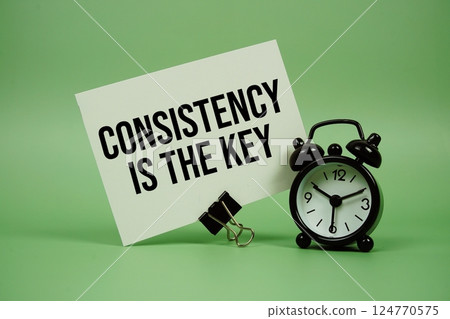 Consistency Is The Key text message on paper card with alarm clock on green background Consistency Is The Key text message on paper card with alarm clock on green background 124770575