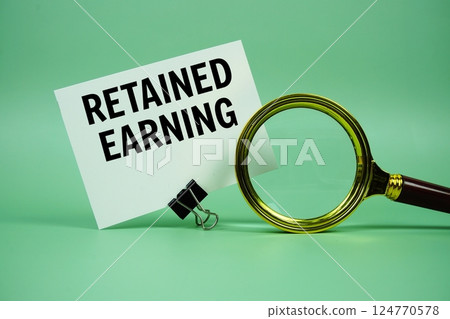Retained Earning text message on paper card with magnifying glass on green background 124770578