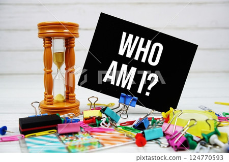 Who am I? text on paper card with hourglass and stationary on wooden background 124770593
