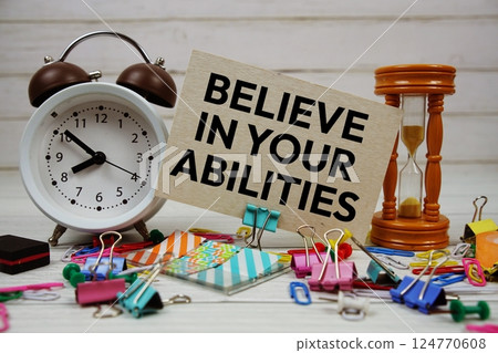 Believe In Your Abilities text on paper card with alarm clock and stationary on wooden background Believe In Your Abilities text on paper card with alarm clock and stationary on wooden background 124770608