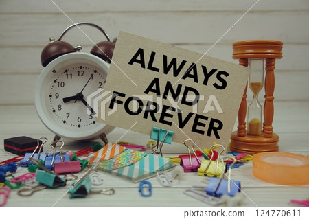 Always And Forever text on paper card with alarm clock and stationary on wooden background 124770611