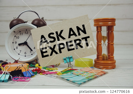 Ask an Expert text on paper card with alarm clock and stationary on wooden background 124770616