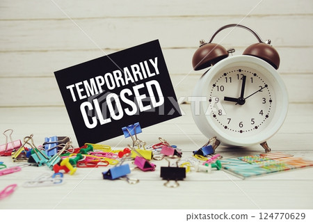 Temporarily Closed text on paper card with alarm clock and stationary on wooden background 124770629