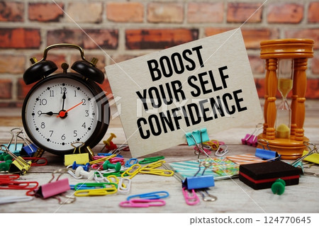 Boost Your Self Confidence text on paper card with alarm clock and stationary on wooden background Boost Your Self Confidence text on paper card with alarm clock and stationary on wooden background 124770645