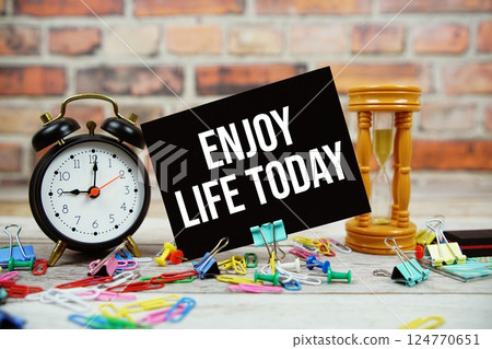 Enjoy Life Today text on paper card with alarm clock and stationary on wooden background Enjoy Life Today text on paper card with alarm clock and stationary on wooden background 124770651