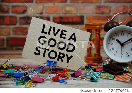Live A Good Story text on paper card with alarm clock and stationary on wooden background Live A Good Story text on paper card with alarm clock and stationary on wooden background 124770668