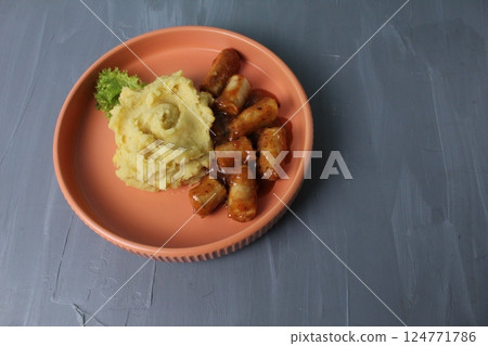 lunch of mashed potatoes and sausages in tomato sauce on a plate on a gray background. Home Food Kitchen Concept lunch of mashed potatoes and sausages in tomato sauce on a plate on a gray background. Home Food Kitchen Concept 124771786