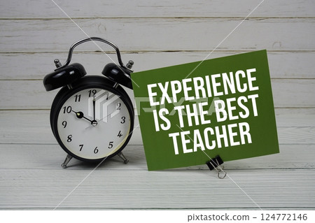 Experience is The Best Teacher text message on paper card with alarm clock on green background 124772146