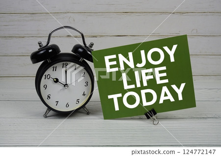 Enjoy Life Today text message on paper card with alarm clock on green background Enjoy Life Today text message on paper card with alarm clock on green background 124772147