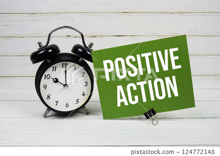 Positive Action text message on paper card with alarm clock on green background 124772148