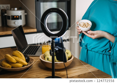 Woman holding a bowl of nuts in front of a ring light, laptop, and healthy food setup. Wellness content creation, digital nutrition coaching, food influencer life, healthy lifestyle branding Woman holding a bowl of nuts in front of a ring light, laptop, and healthy food setup. Wellness content creation, digital nutrition coaching, food influencer life, healthy lifestyle branding 124772558