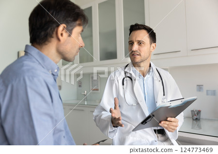 Hispanic middle-aged doctor consulting patient during visit in clinic 124773469