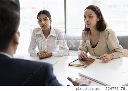 Two multiracial young and mature women colleagues participate in briefing Two multiracial young and mature women colleagues participate in briefing 124773476