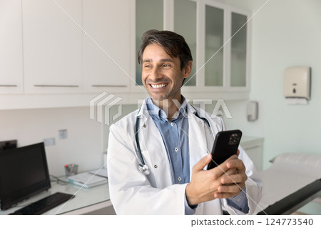 Happy male doctor using phone in workplace 124773540