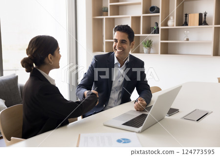 Indian older and younger businesspeople shaking hands seated at table 124773595