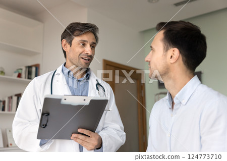 Man cardiologist holds clipboard, engaged in friendly conversation with patient 124773710
