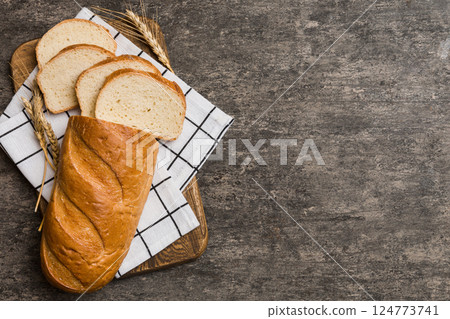 Freshly baked bread slices on cutting board against white wooden background. top view Sliced bread 124773741