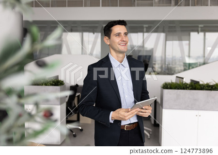 Positive pensive Latin manager man holding tablet computer in office Positive pensive Latin manager man holding tablet computer in office 124773896