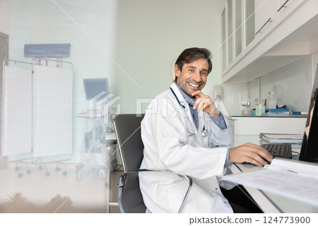 Portrait of smiling doctor sits at desk in medical office Portrait of smiling doctor sits at desk in medical office 124773900