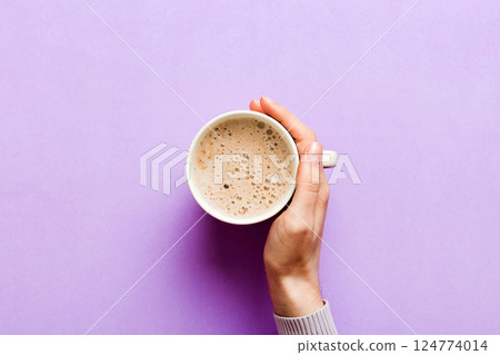 Minimalistic style woman hand holding a cup of coffee on Colored background. Flat lay, top view cappuccino cup. Empty place for text, copy space. Coffee addiction. Top view, flat lay 124774014