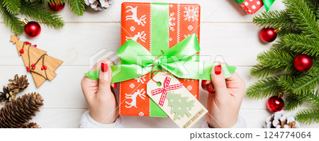 Top view of female hand tie up New Year present on festive wooden background. Fir tree and holiday decorations. Christmas time concept Top view of female hand tie up New Year present on festive wooden background. Fir tree and holiday decorations. Christmas time concept 124774064