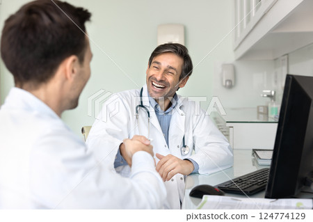 Two physicians shaking hands seated at desk in clinic office 124774129