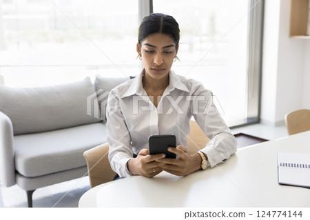 Indian office employee focused on her smartphone seated at desk 124774144