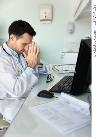GP take break seated at desk in clinic office 124774153
