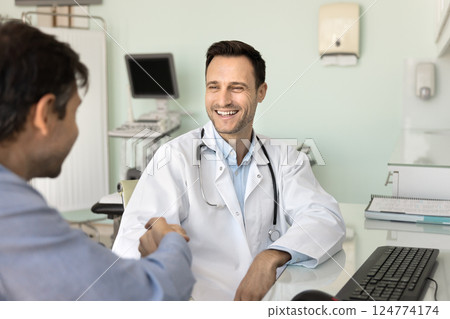 Smiling doctor and happy male patient shaking hands during appointment 124774174