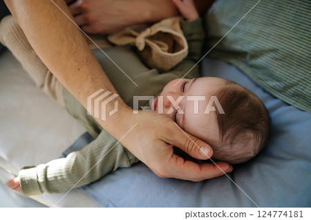 Father putting the baby to sleep, lying next to him in the crib. 124774181