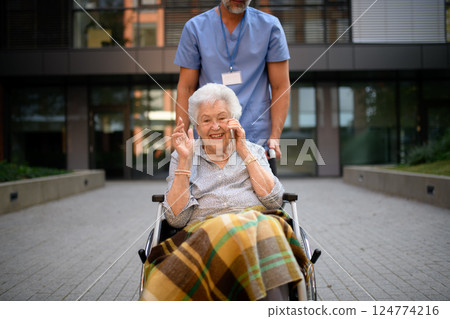 Male caregiver pushing senior woman in wheelchair. Male caregiver pushing senior woman in wheelchair. 124774216