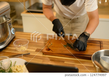 Close up of man wearing black gloves chopping herbs on a wooden cutting board 124774997