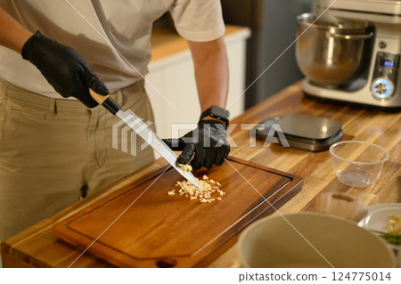 Close up of man chopping garlic on wooden cutting board in a modern kitchen 124775014
